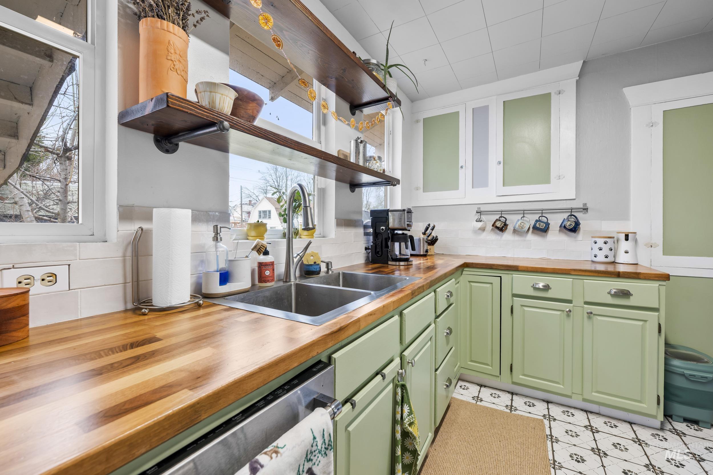Kitchen with wood counters, open shelves, green cabinets, light flooring, and dishwasher