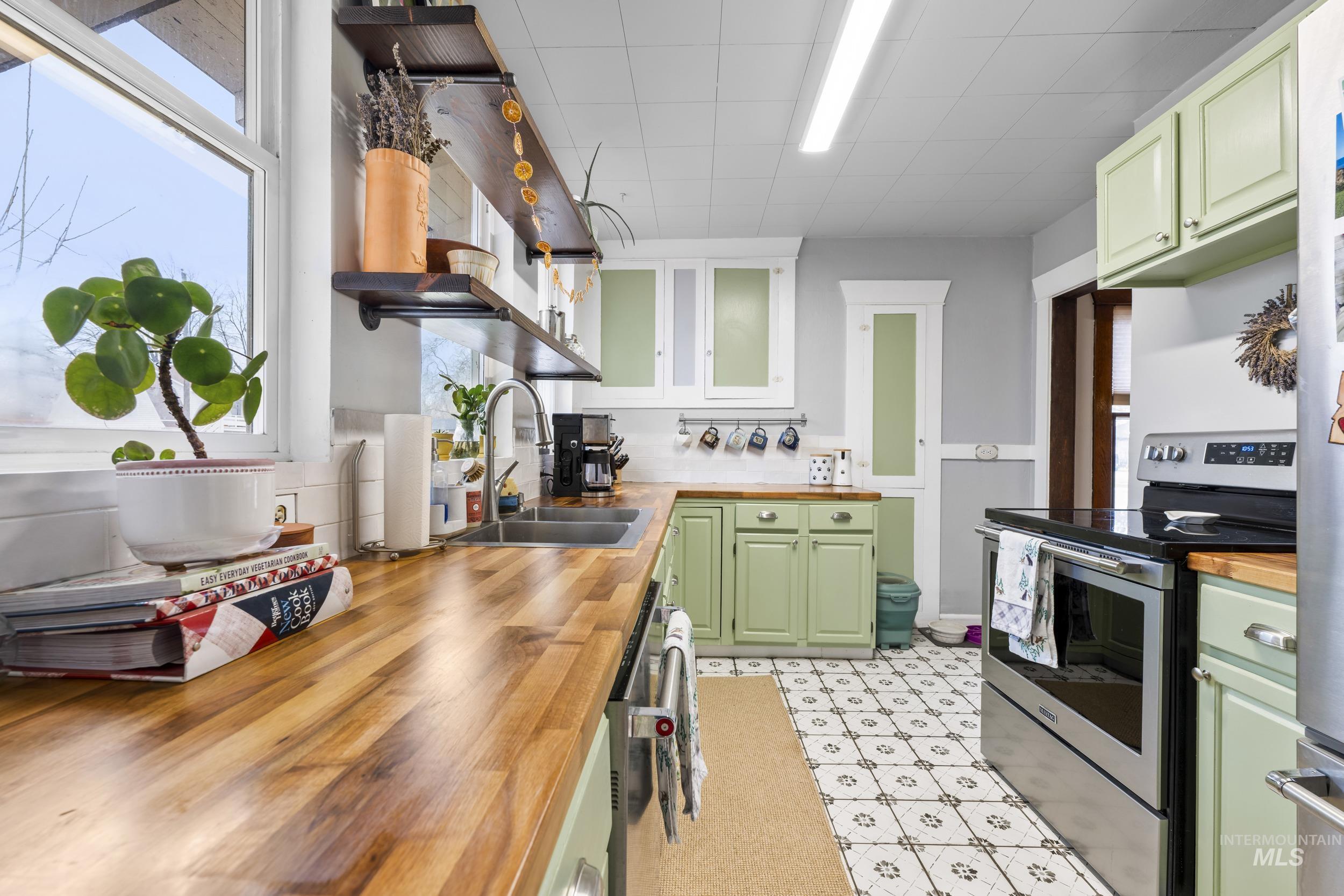 Kitchen with green cabinets, wood counters, stainless steel appliances, open shelves, and glass insert cabinets