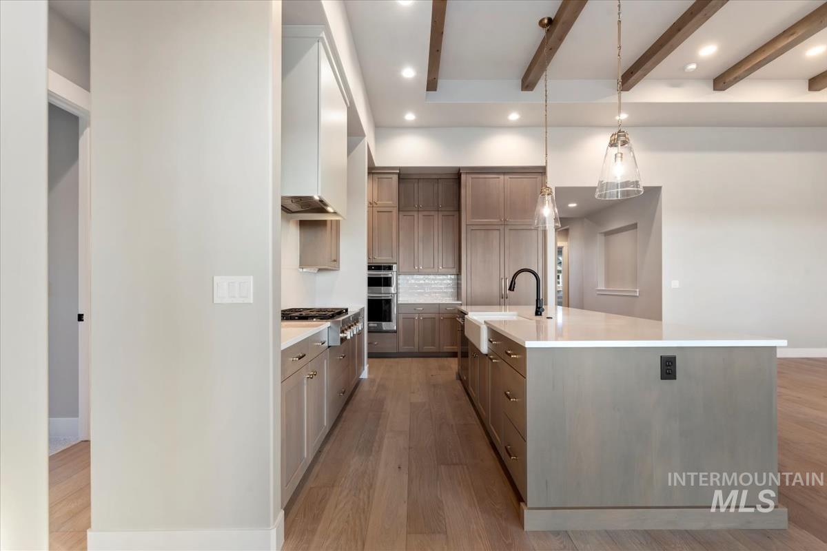 Kitchen with beamed ceiling, decorative backsplash, hanging light fixtures, a large island, and light wood-style flooring