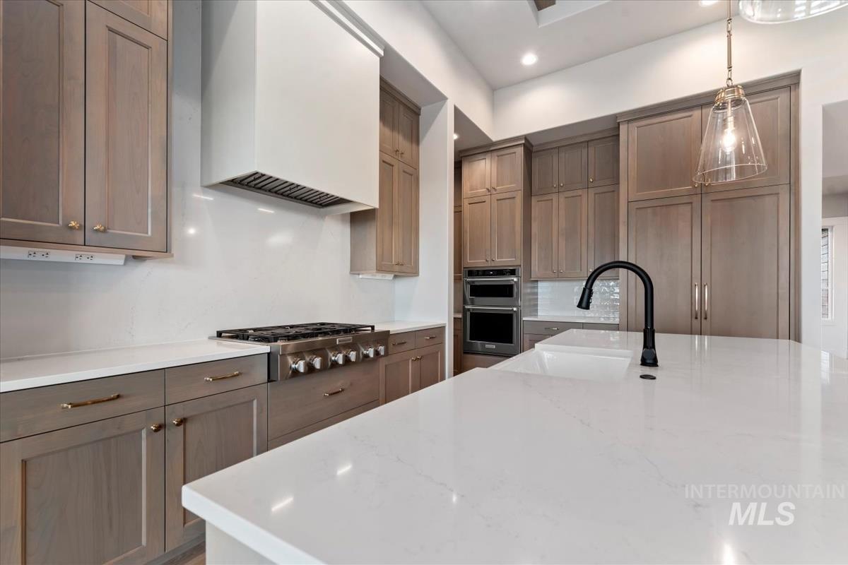 Kitchen featuring premium range hood, light stone countertops, appliances with stainless steel finishes, hanging light fixtures, and recessed lighting
