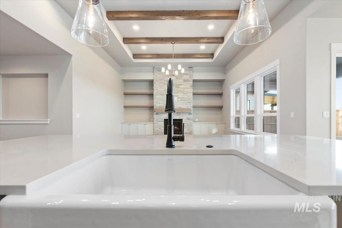 Kitchen view of beamed ceiling, light stone countertops, a chandelier, a fireplace, and recessed lighting