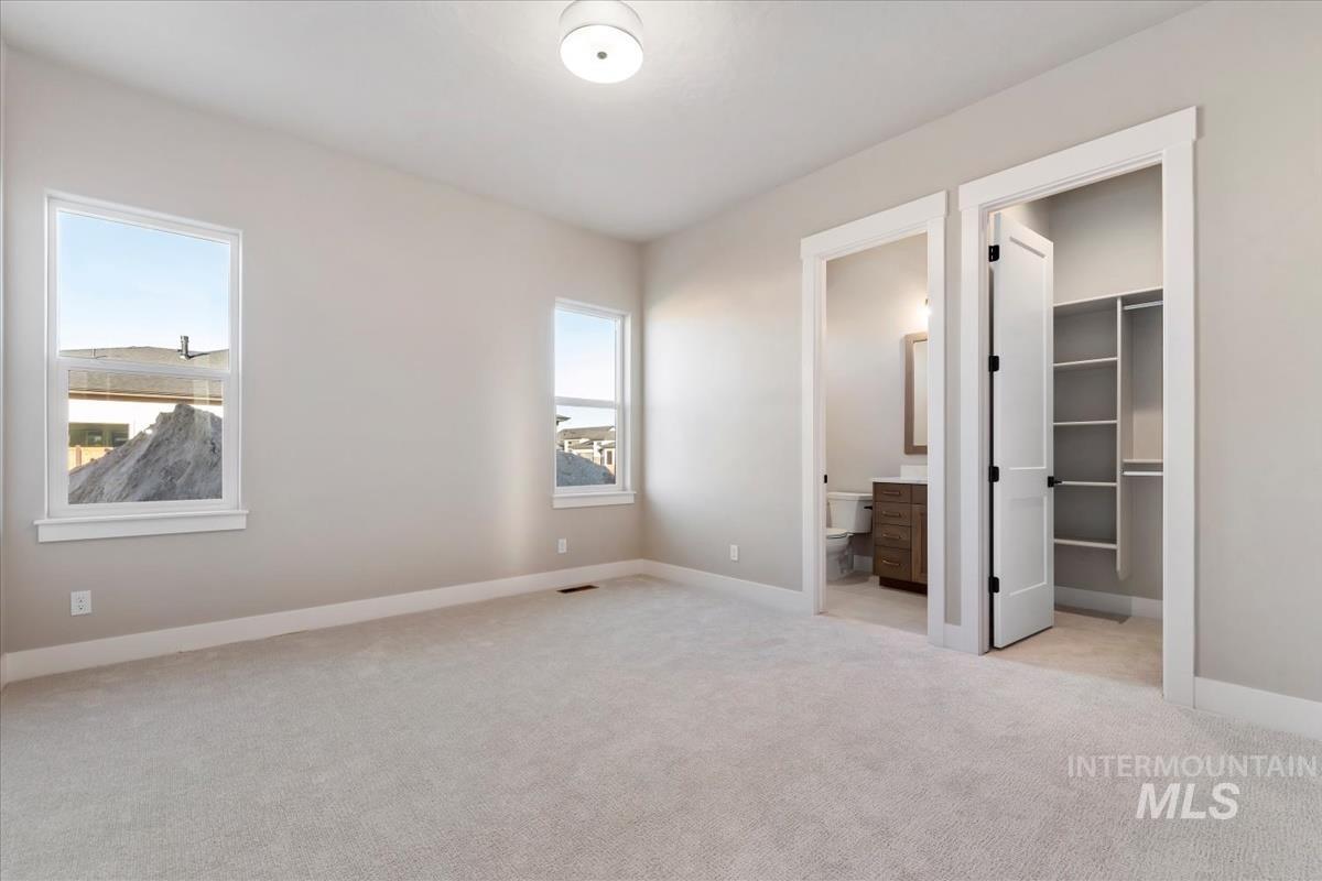Unfurnished bedroom featuring a walk in closet, light colored carpet, and connected bathroom