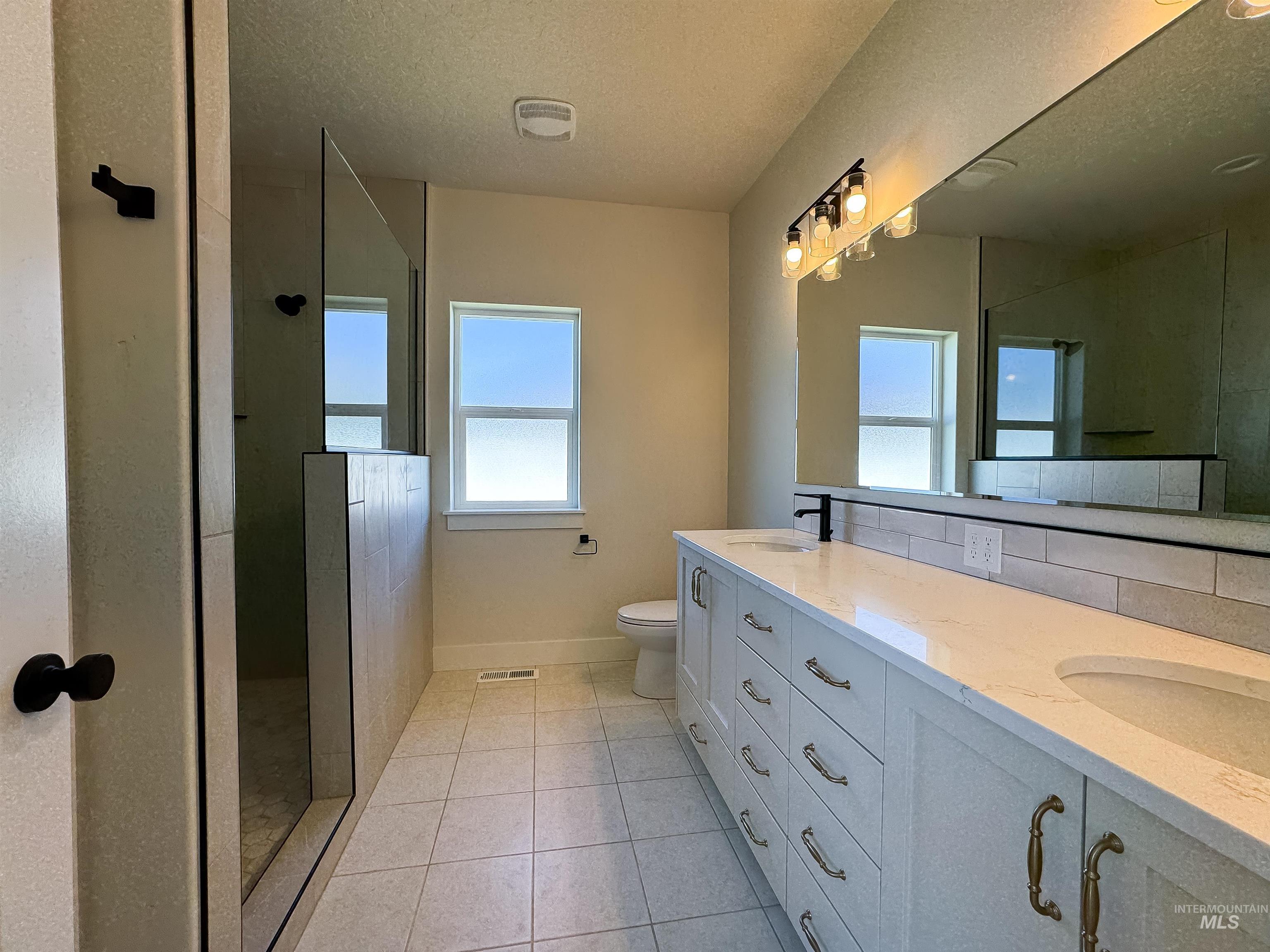 Bathroom with a textured ceiling, double vanity, a walk in shower, tile patterned flooring, and backsplash