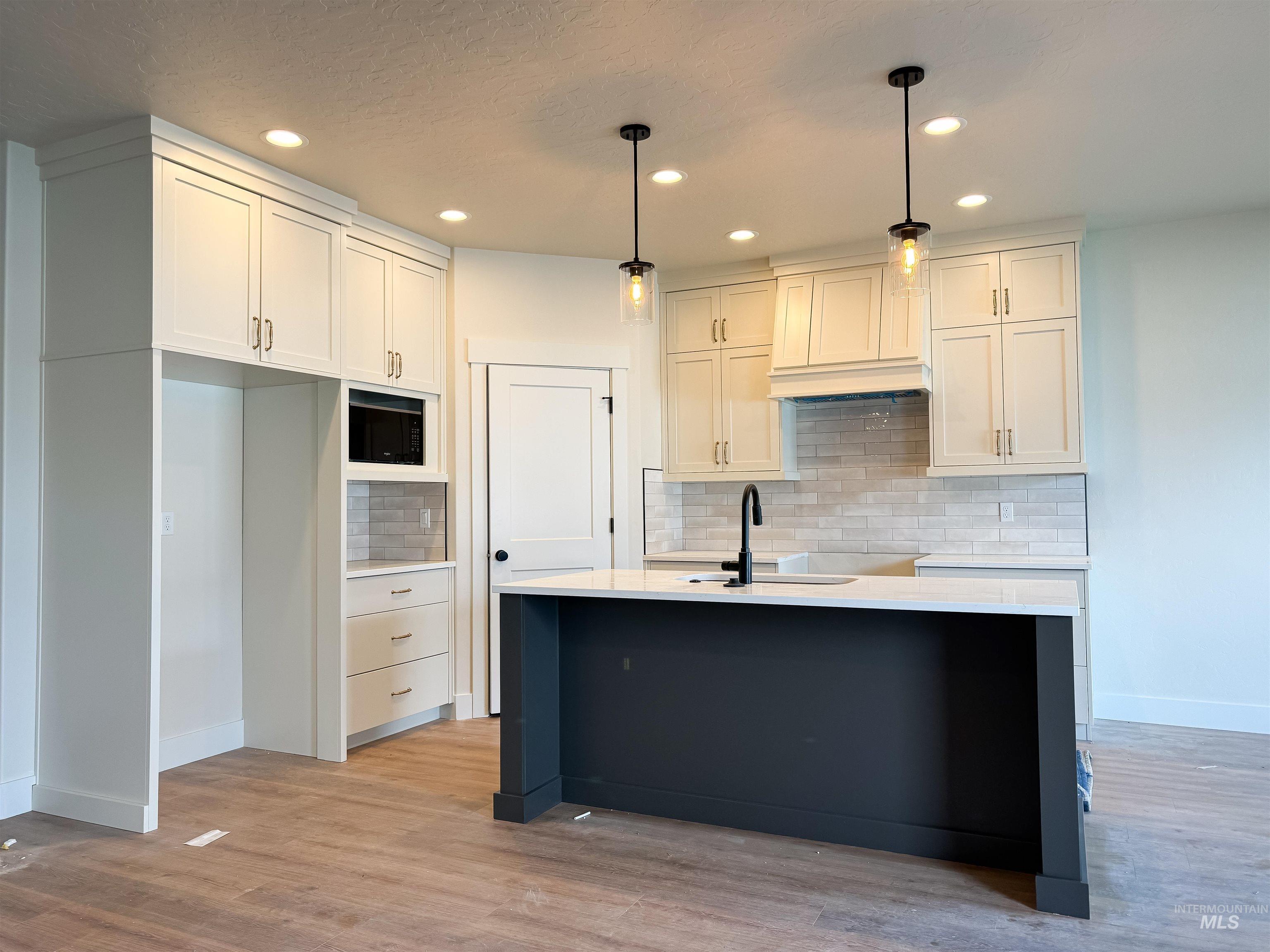 Kitchen with decorative backsplash, recessed lighting, light wood-style flooring, decorative light fixtures, and a kitchen island with sink