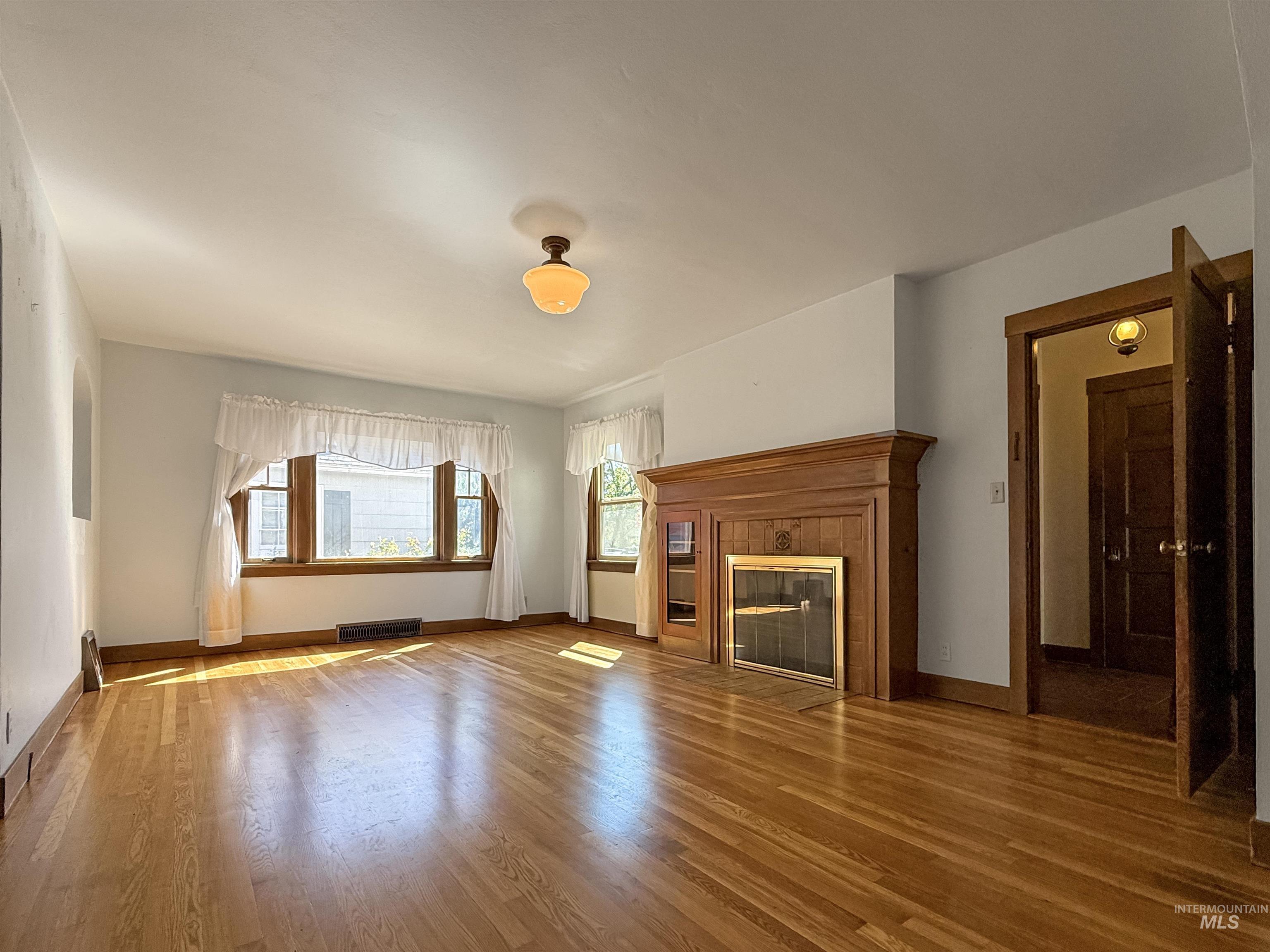 Unfurnished living room with wood finished floors and a tiled fireplace