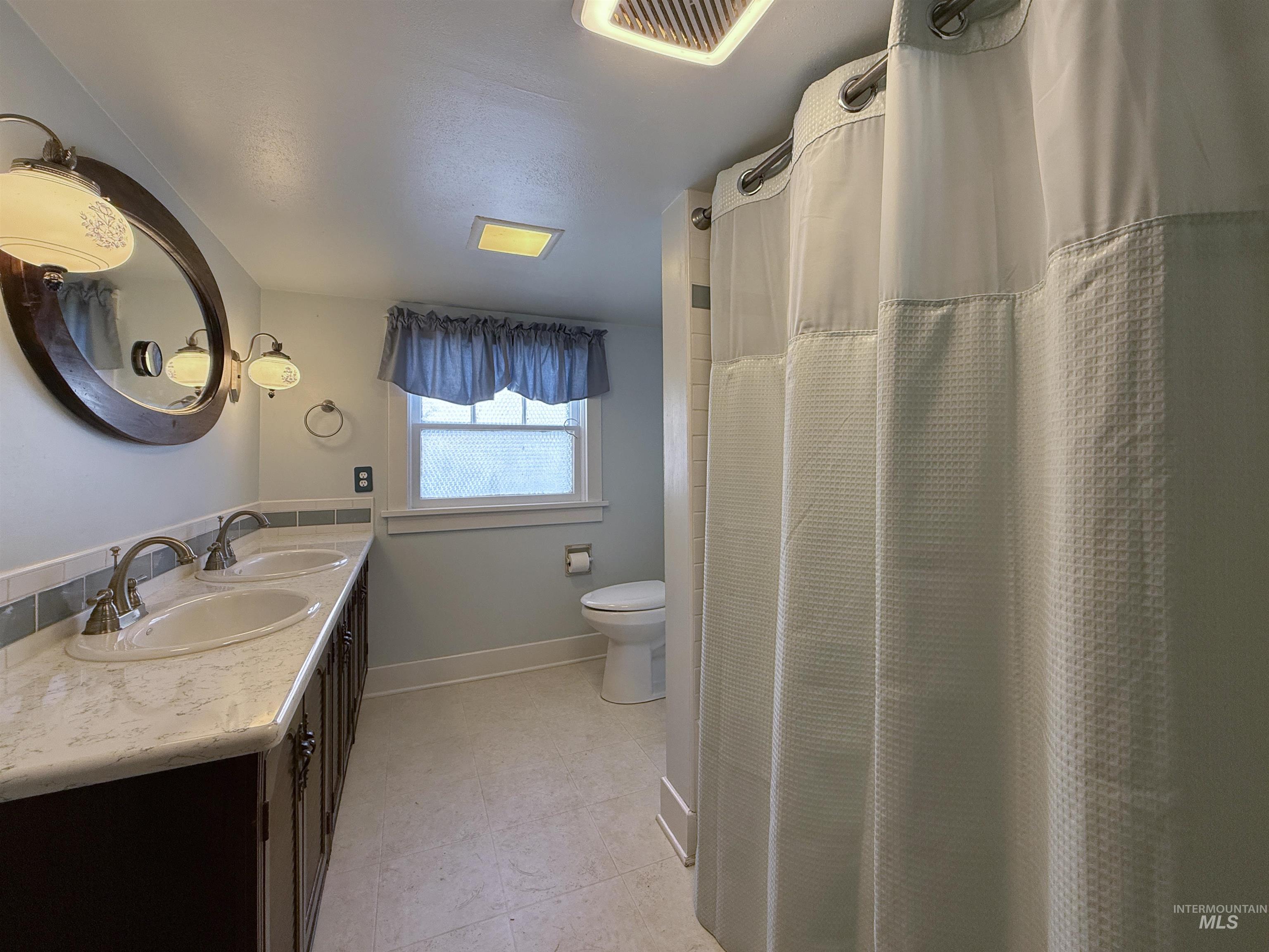 Full bathroom with double vanity, light tile patterned floors, and a shower with curtain