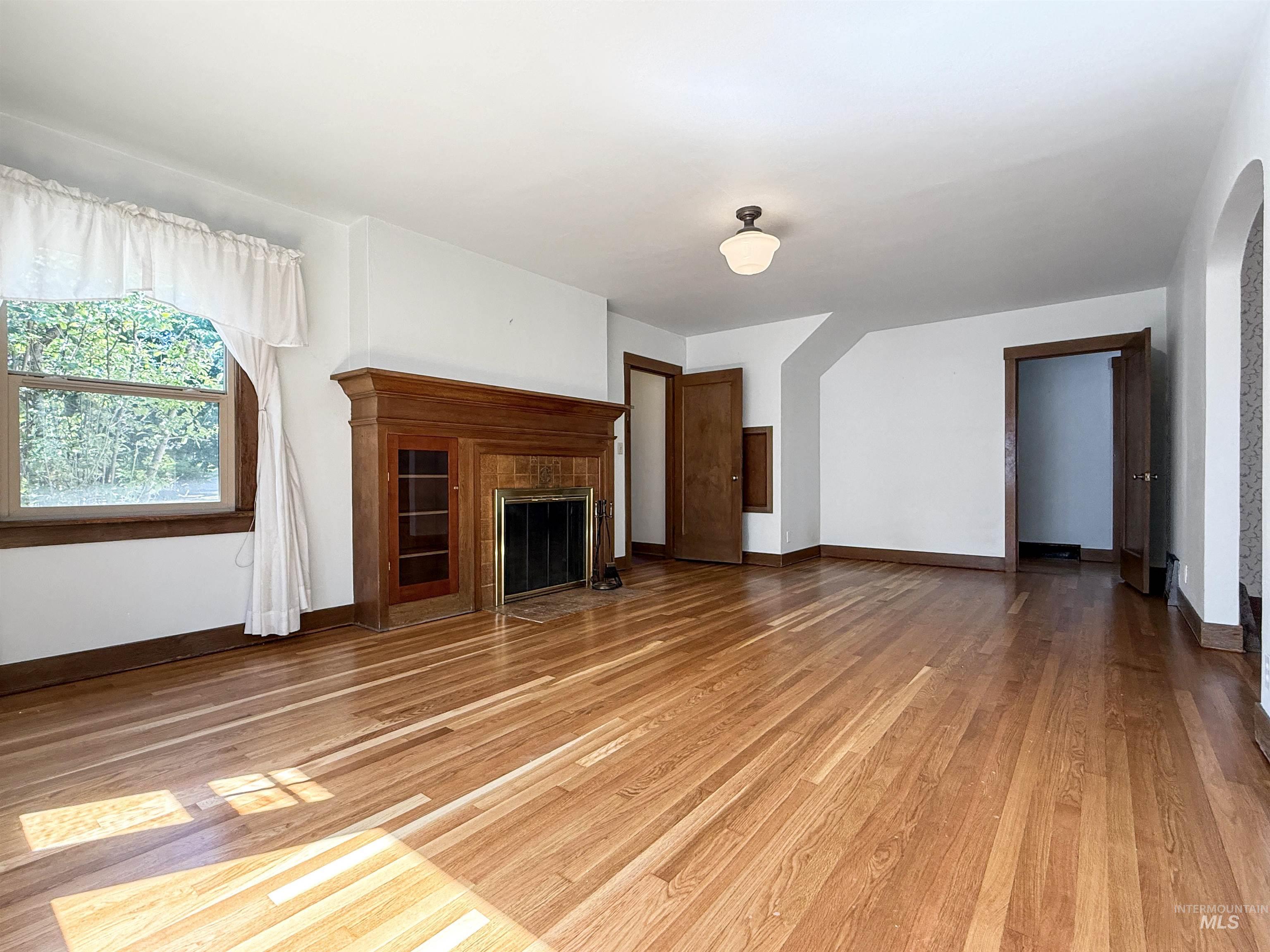 Unfurnished living room with a fireplace with flush hearth, light wood-type flooring, and arched walkways