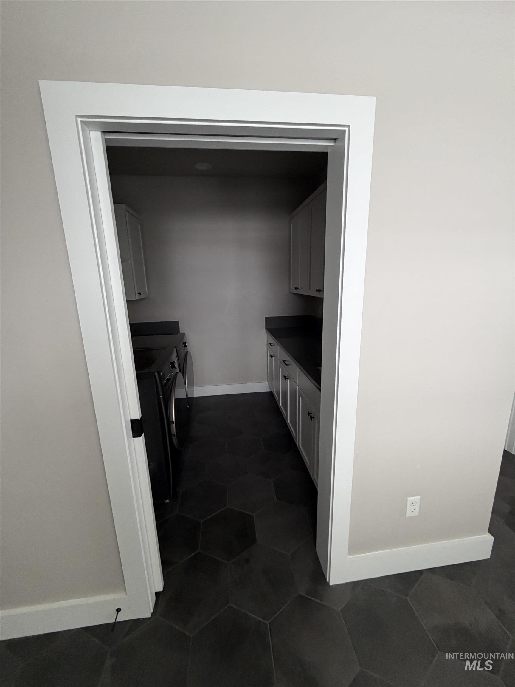 Washroom featuring independent washer and dryer, dark tile patterned floors, and cabinet space
