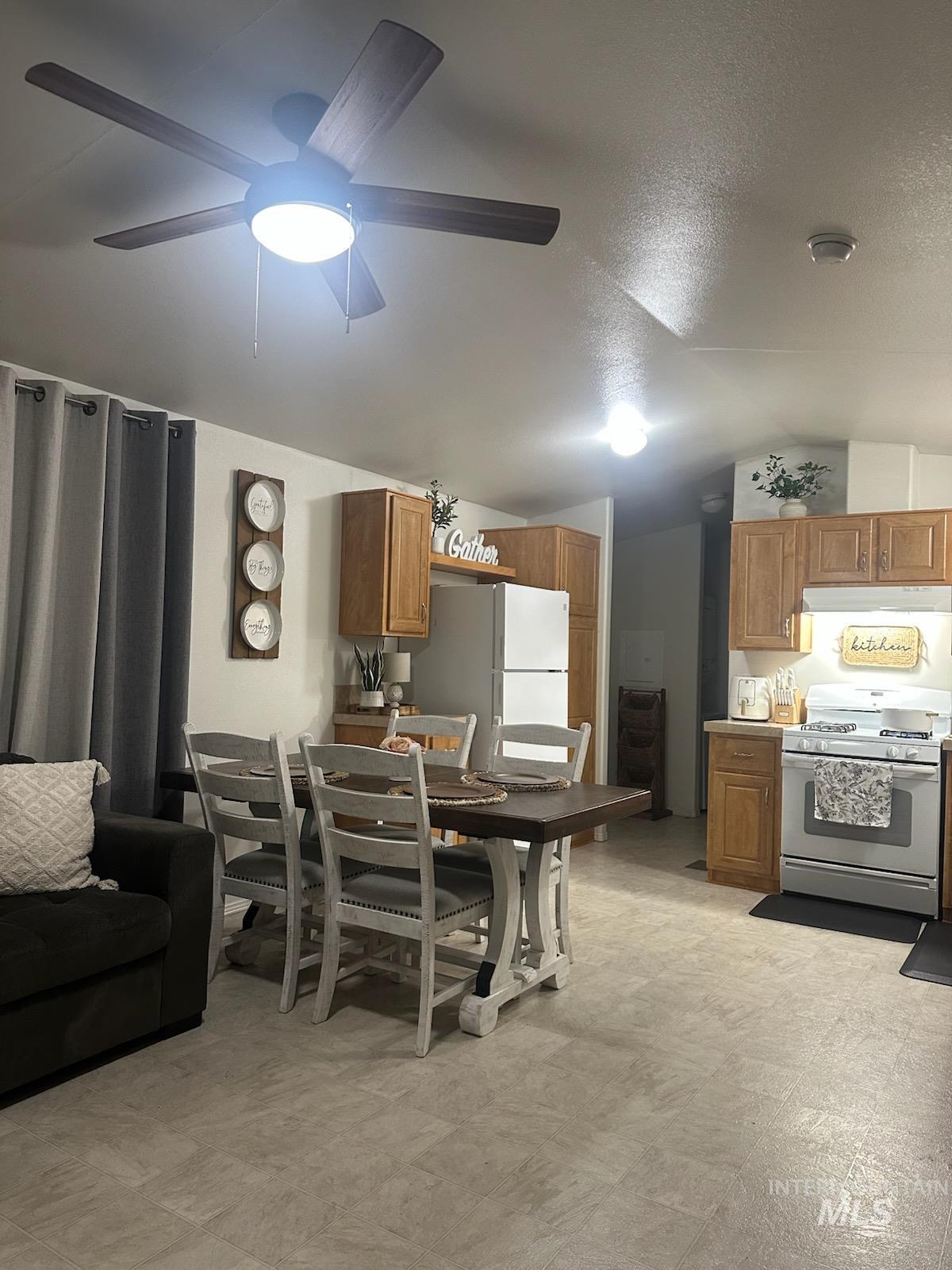 Dining area with vaulted ceiling, light flooring, a textured ceiling, and ceiling fan