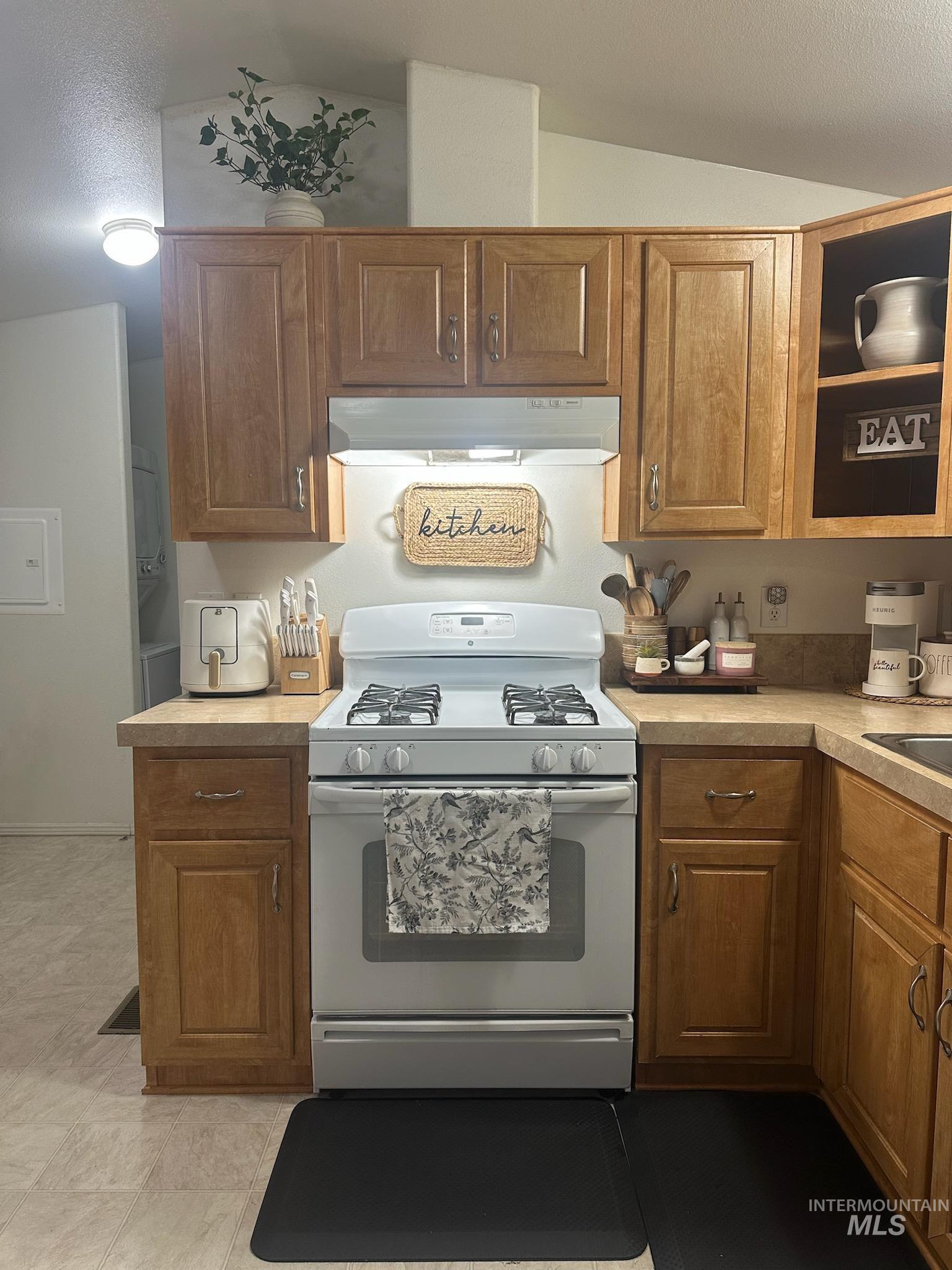 Kitchen featuring white gas range oven, under cabinet range hood, light countertops, a textured ceiling, and brown cabinetry