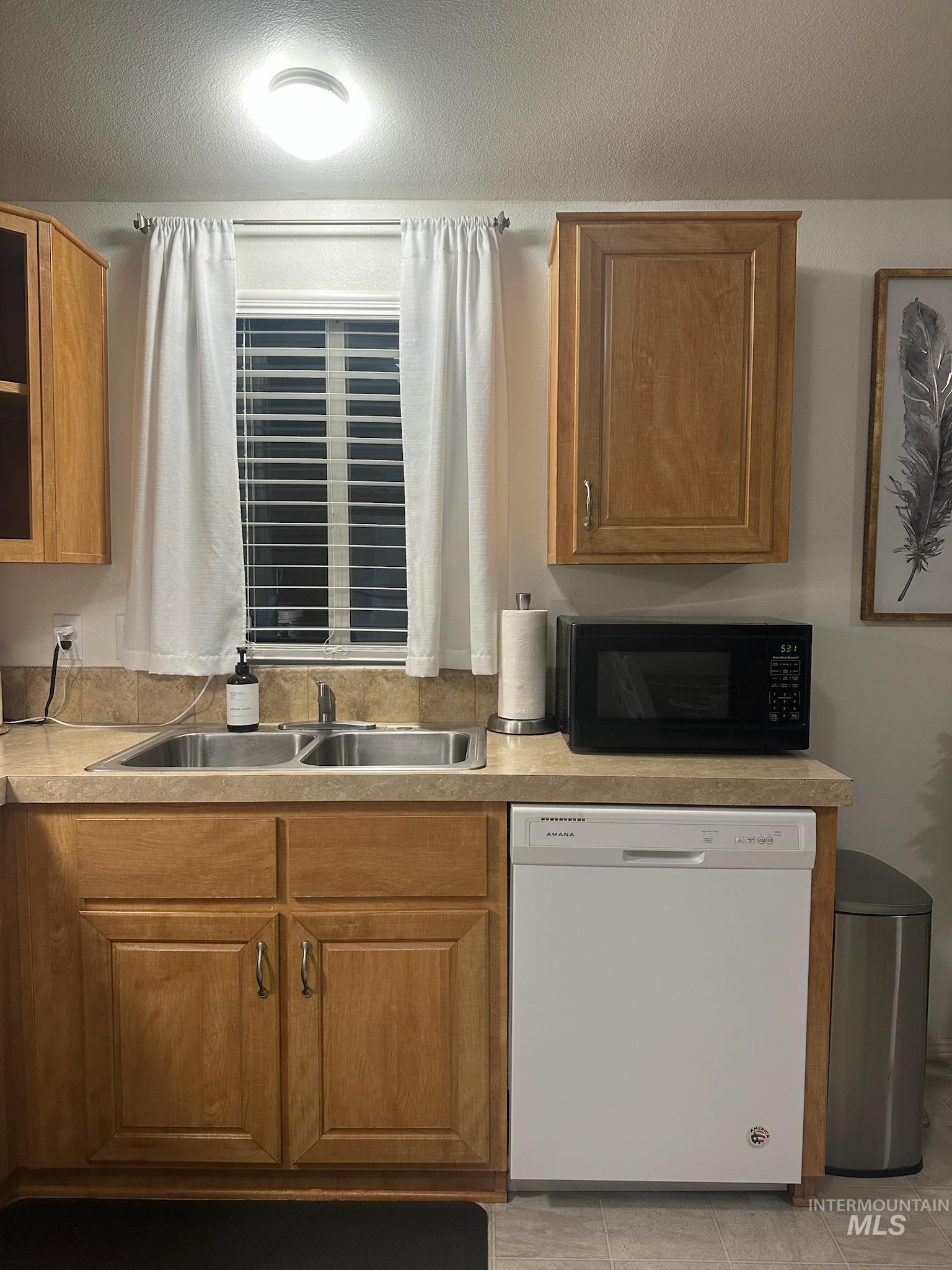 Kitchen with white dishwasher, brown cabinetry, light countertops, black microwave, and a textured ceiling