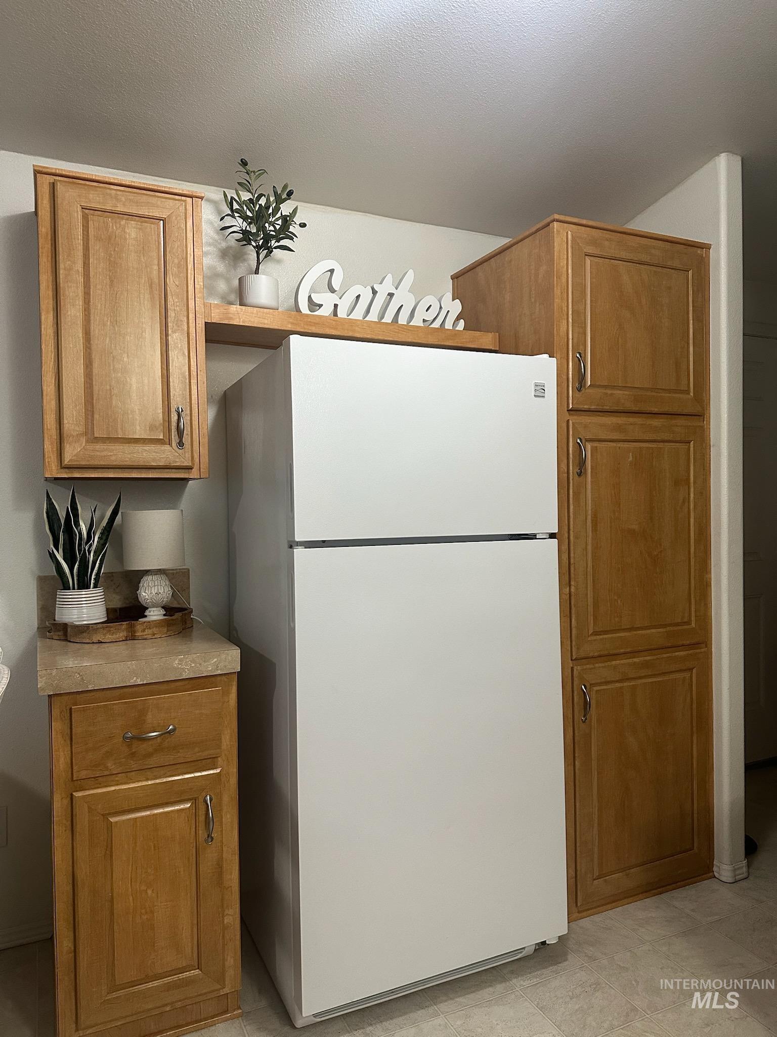 Kitchen with freestanding refrigerator, brown cabinetry, light countertops, and a textured ceiling