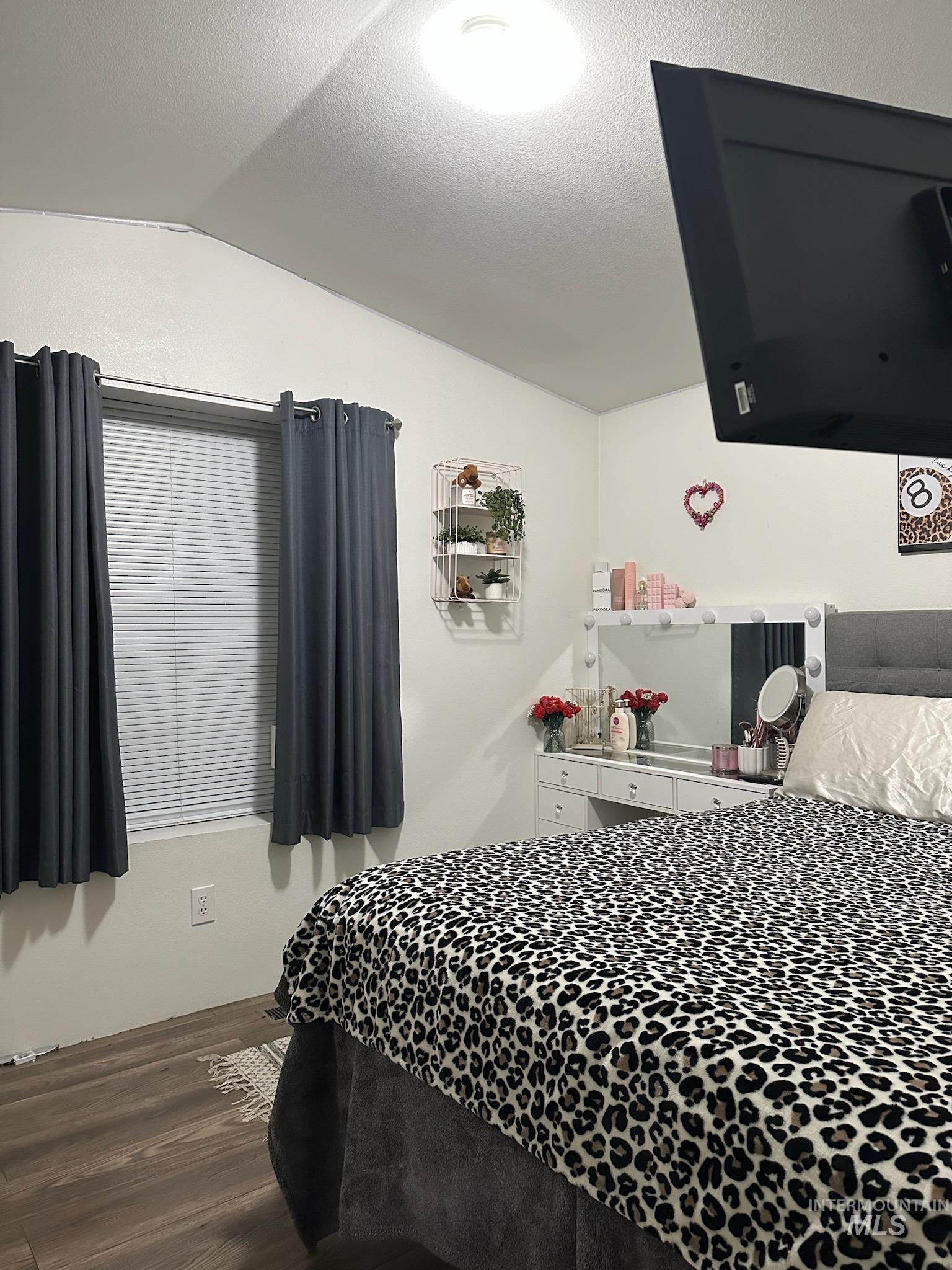 Bedroom featuring vaulted ceiling, a textured ceiling, and wood finished floors