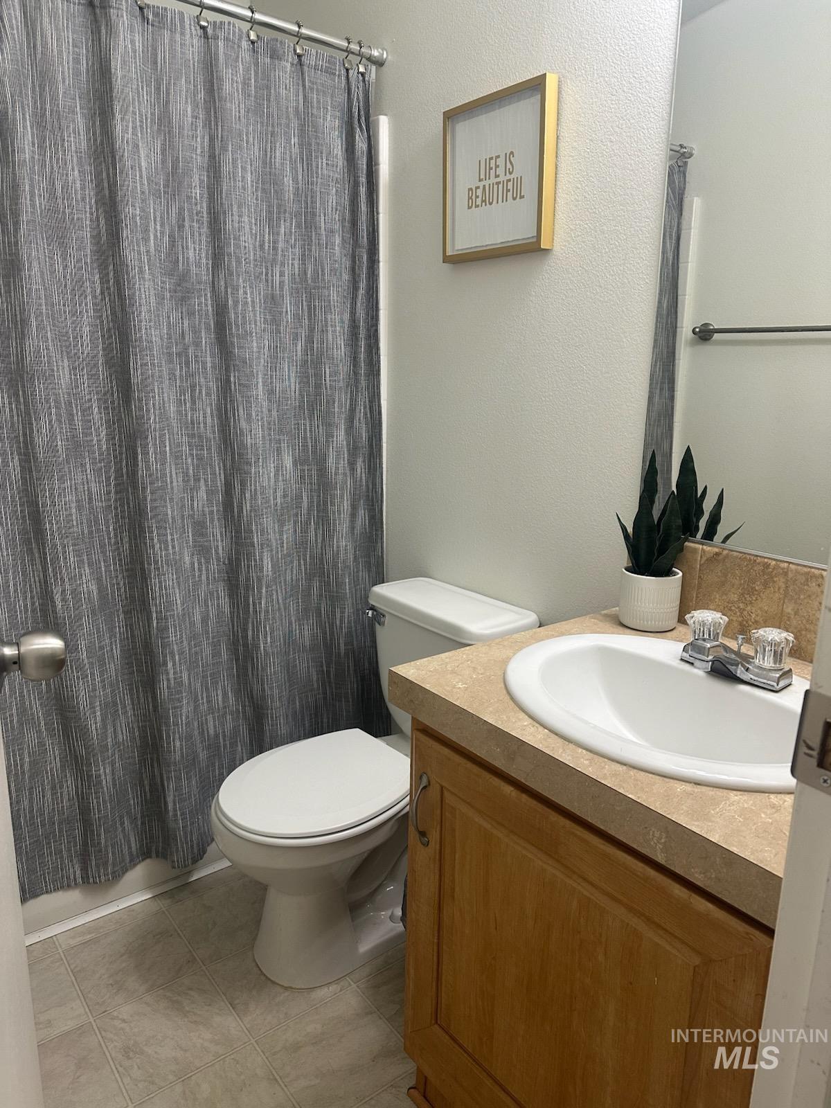 Bathroom with vanity, curtained shower, a textured wall, and light tile patterned flooring