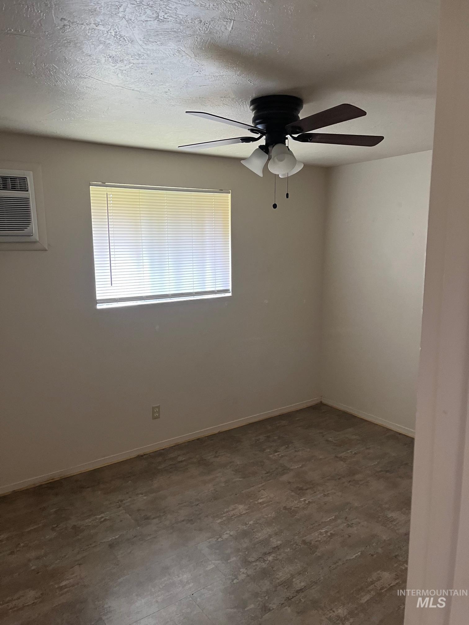 Unfurnished room featuring unfinished concrete flooring, a textured ceiling, an AC wall unit, and a ceiling fan