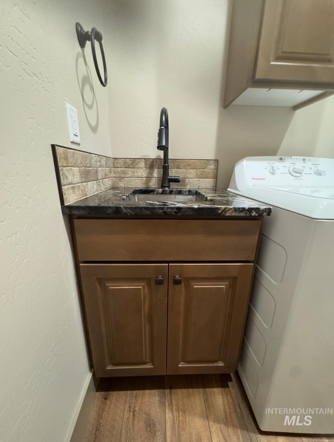 Washroom with washer / dryer, a textured wall, light wood-style flooring, and cabinet space