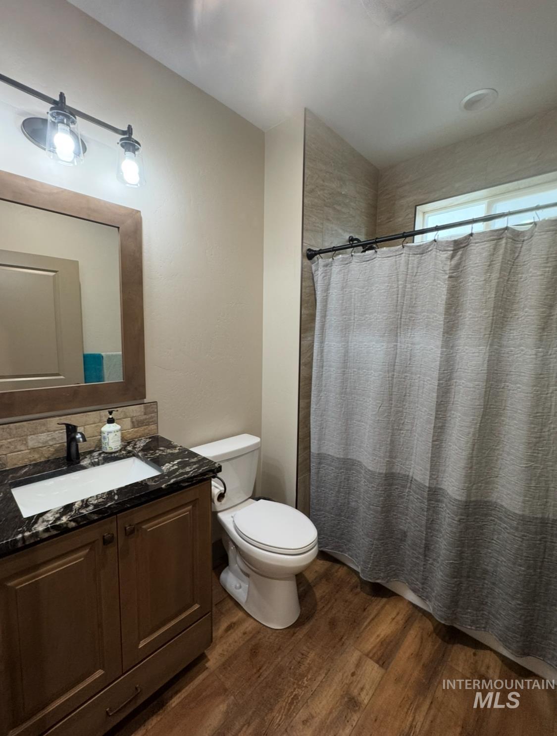 Full bathroom featuring a shower with curtain, vanity, dark wood-style floors, and backsplash
