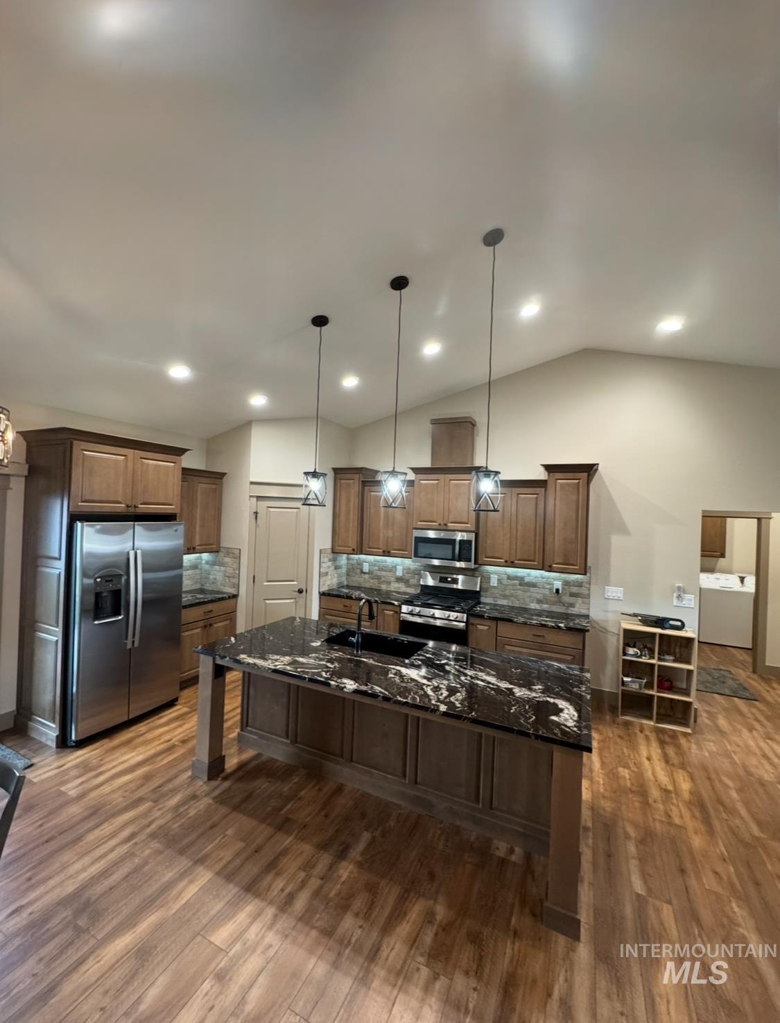 Kitchen with backsplash, dark stone counters, stainless steel appliances, a center island with sink, and a kitchen breakfast bar