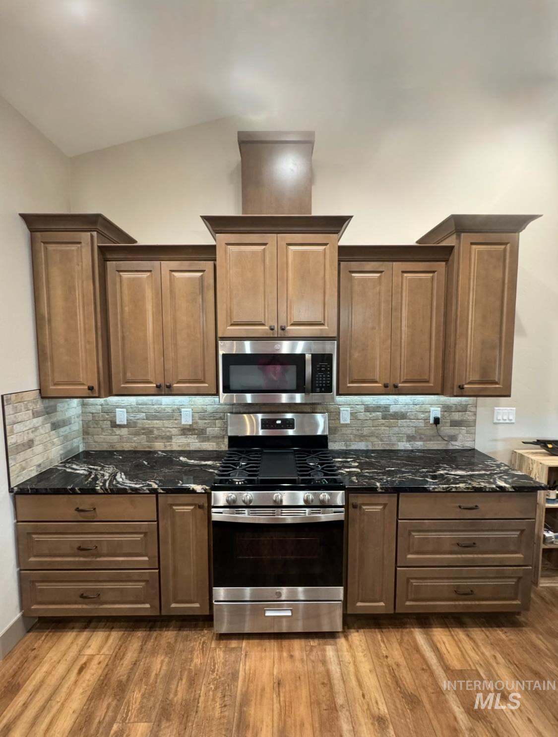 Kitchen with dark stone countertops, stainless steel appliances, tasteful backsplash, and light wood-type flooring