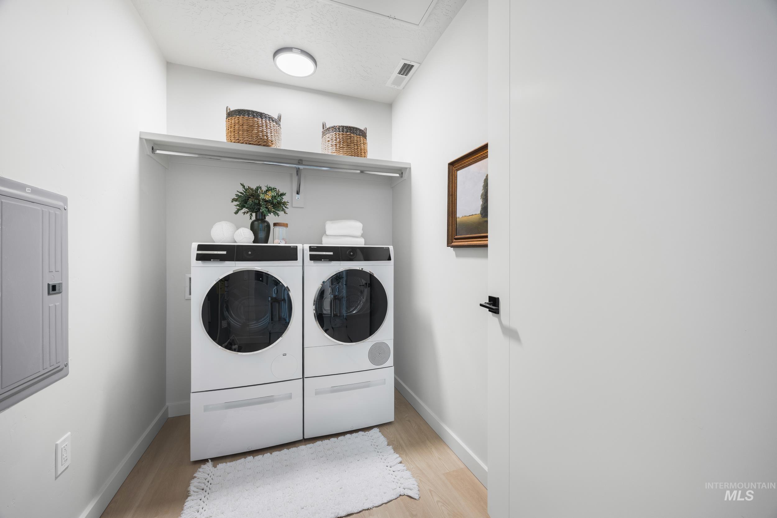 Washroom with washing machine and clothes dryer, light wood finished floors, electric panel, and a textured ceiling
