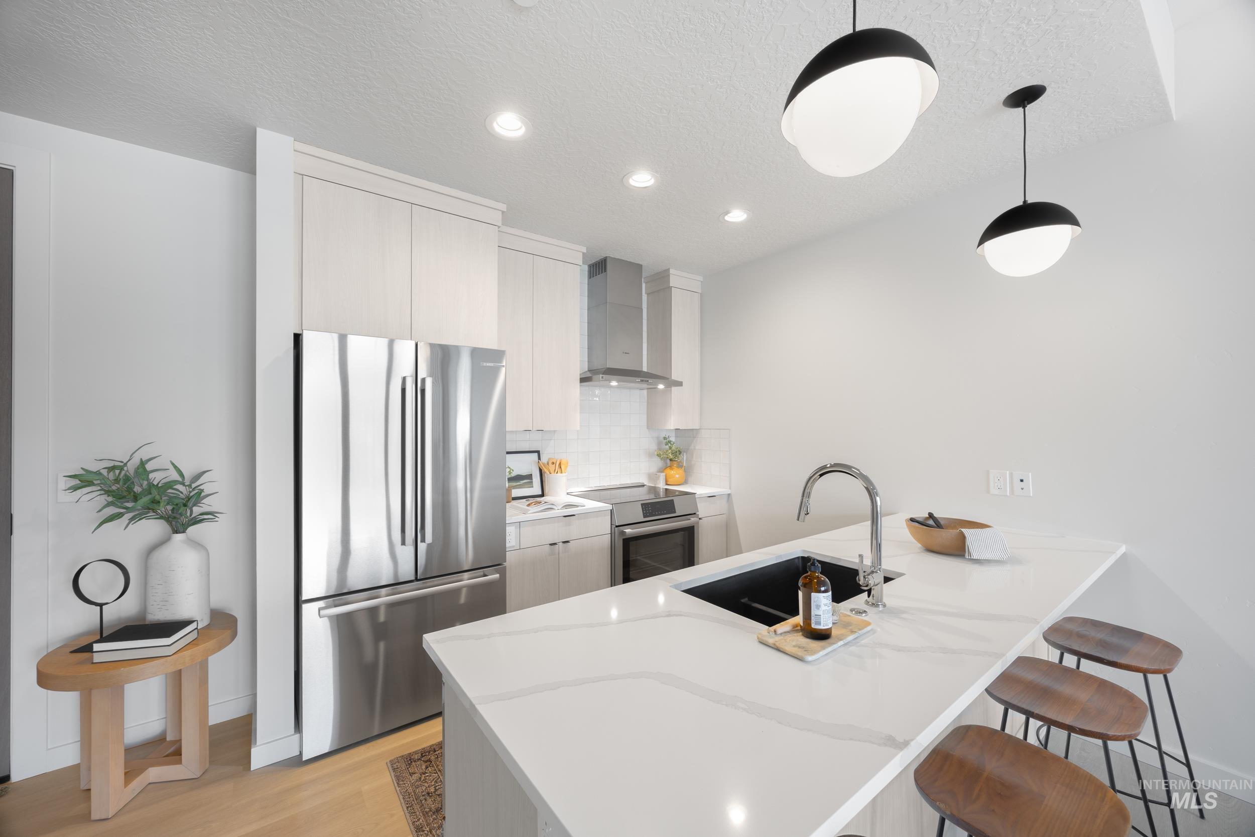 Kitchen with appliances with stainless steel finishes, a breakfast bar area, a peninsula, decorative backsplash, and wall chimney exhaust hood