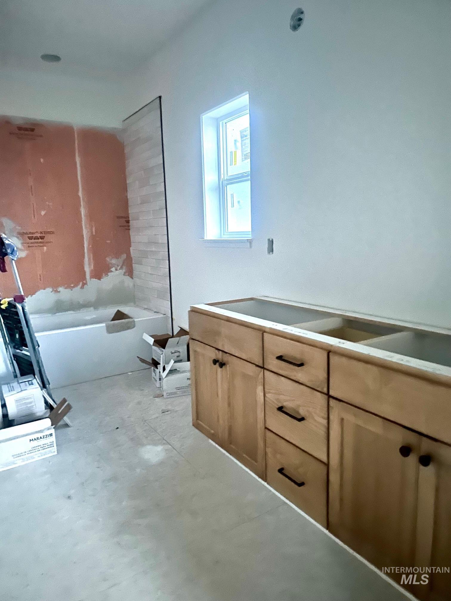 Bathroom featuring a bathtub, double vanity, and concrete flooring