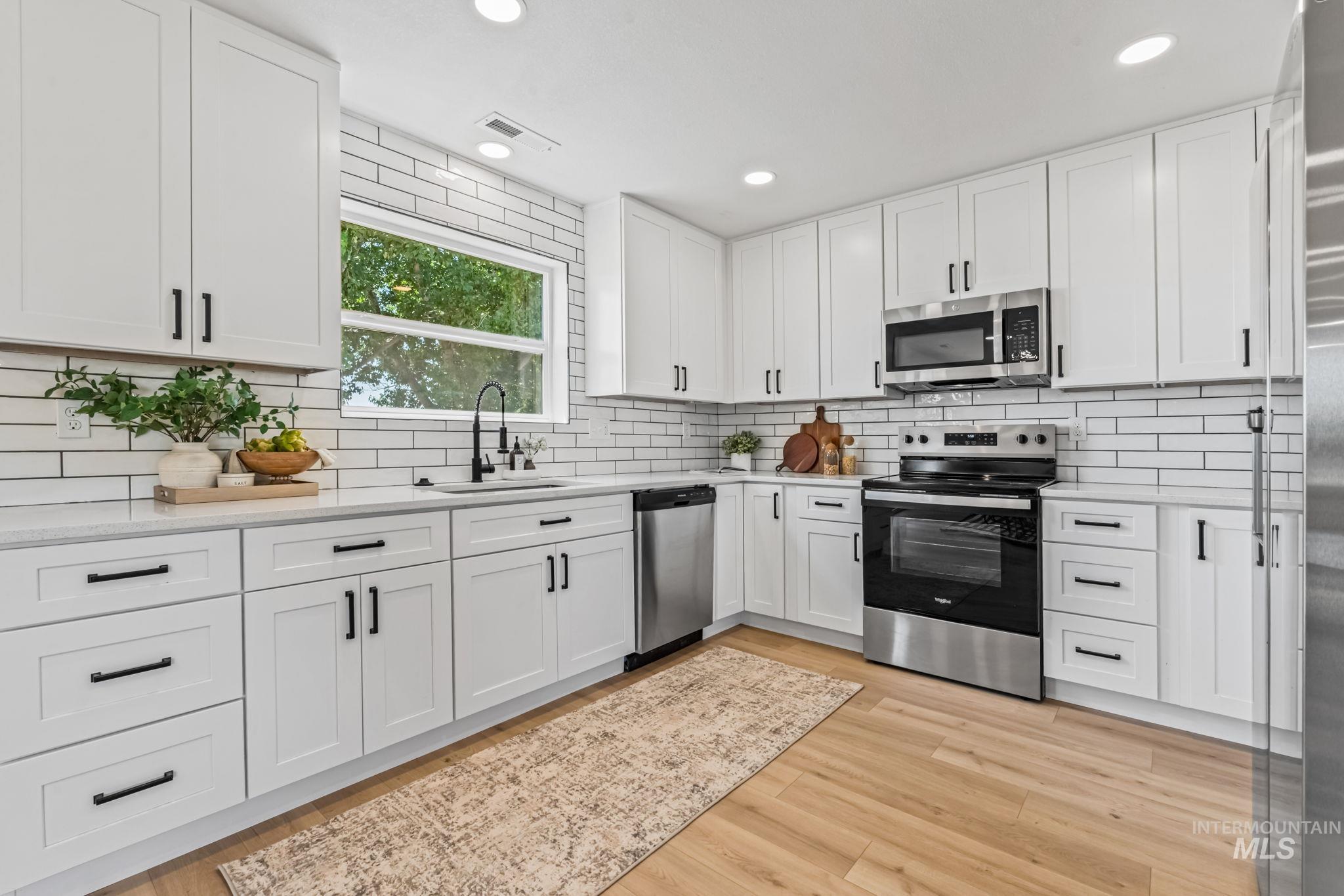 Kitchen featuring appliances with stainless steel finishes, white cabinets, light stone countertops, light wood finished floors, and recessed lighting