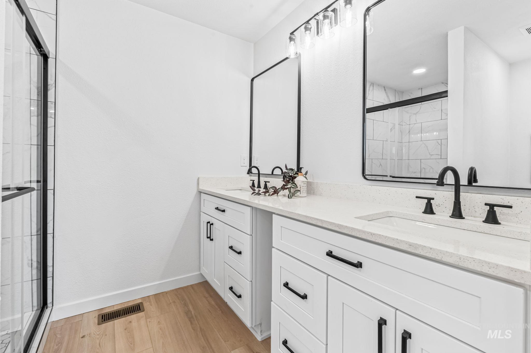 Bathroom with a shower stall, light wood-style floors, and double vanity