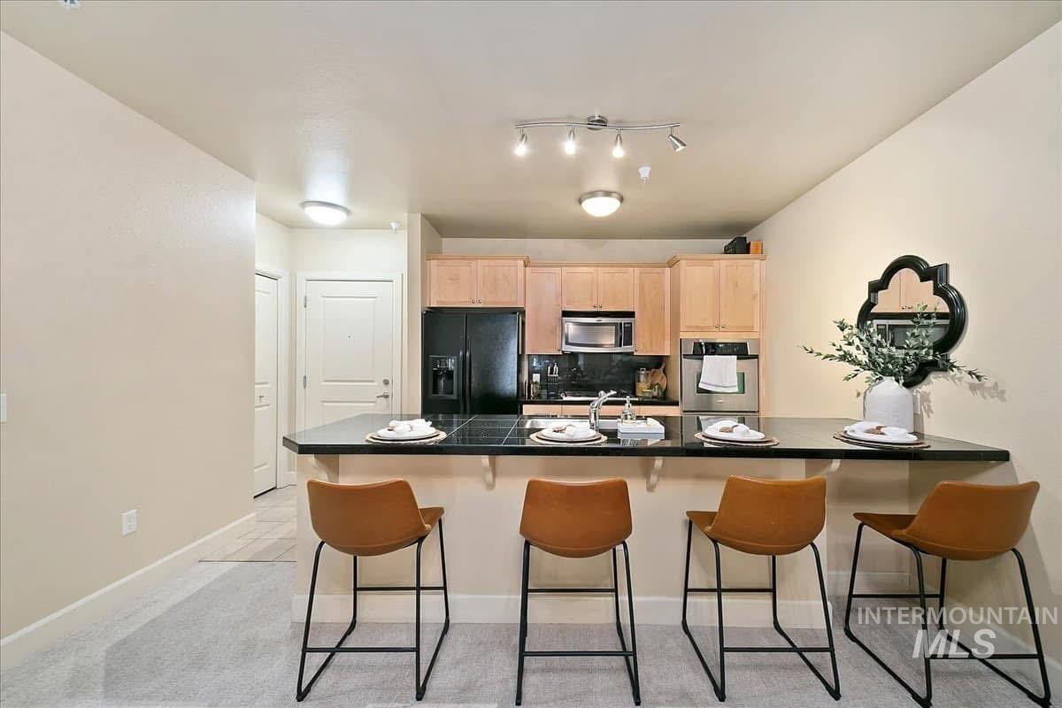 Kitchen featuring light brown cabinetry, stainless steel appliances, a peninsula, decorative backsplash, and a kitchen bar