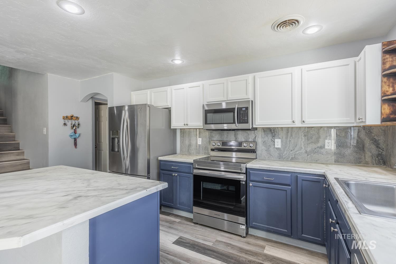 Kitchen with blue cabinets, open shelves, appliances with stainless steel finishes, white cabinetry, and recessed lighting