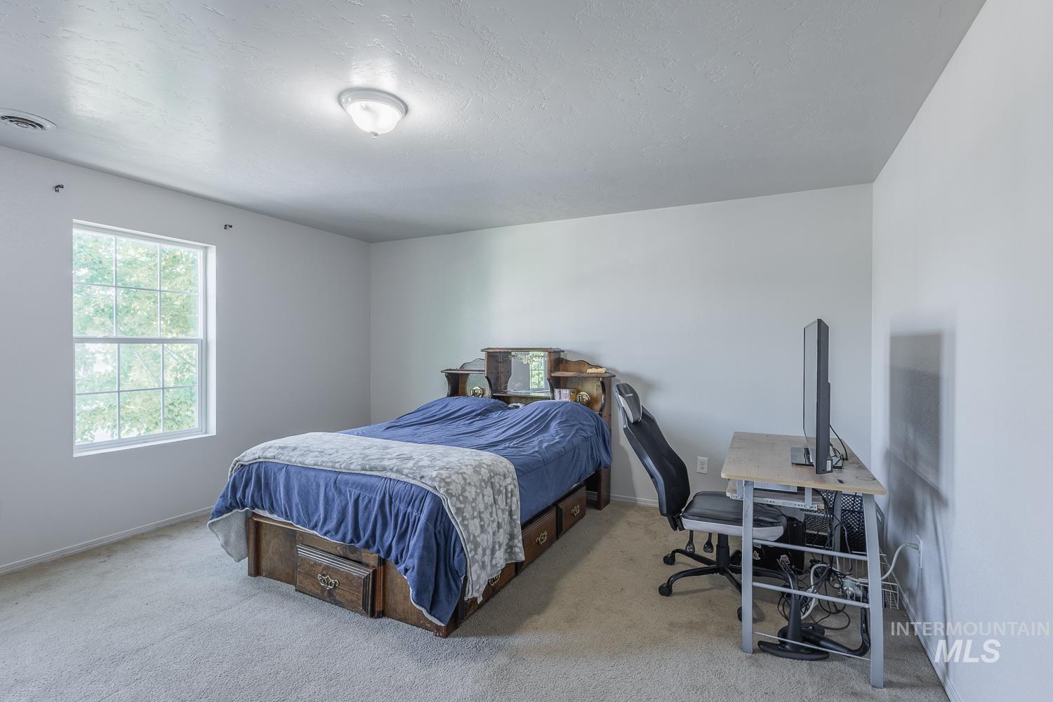 Bedroom with light colored carpet, a textured ceiling, and an office area