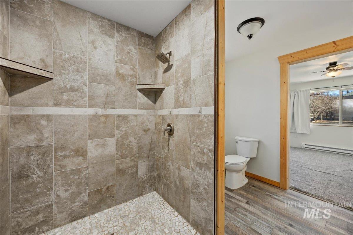 Full bathroom featuring tiled shower, wood finished floors, ceiling fan, and baseboard heating