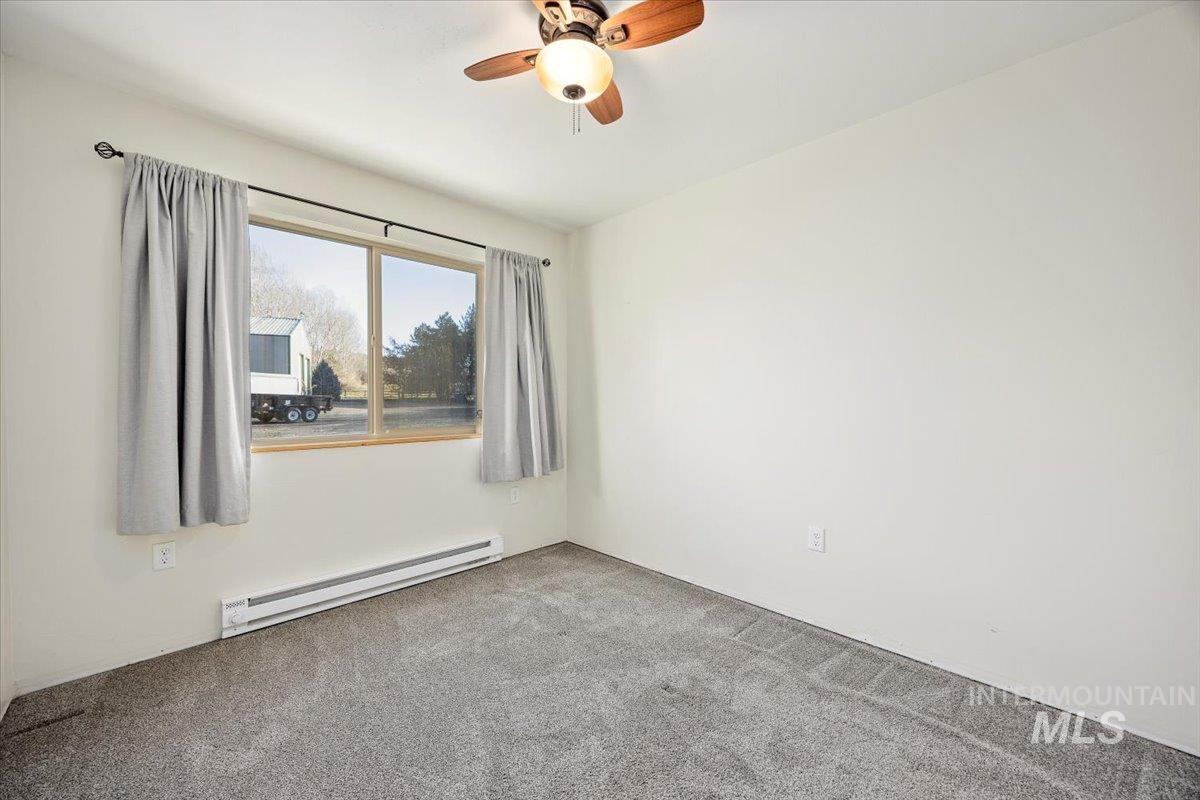 Unfurnished room featuring baseboard heating, carpet, and a ceiling fan