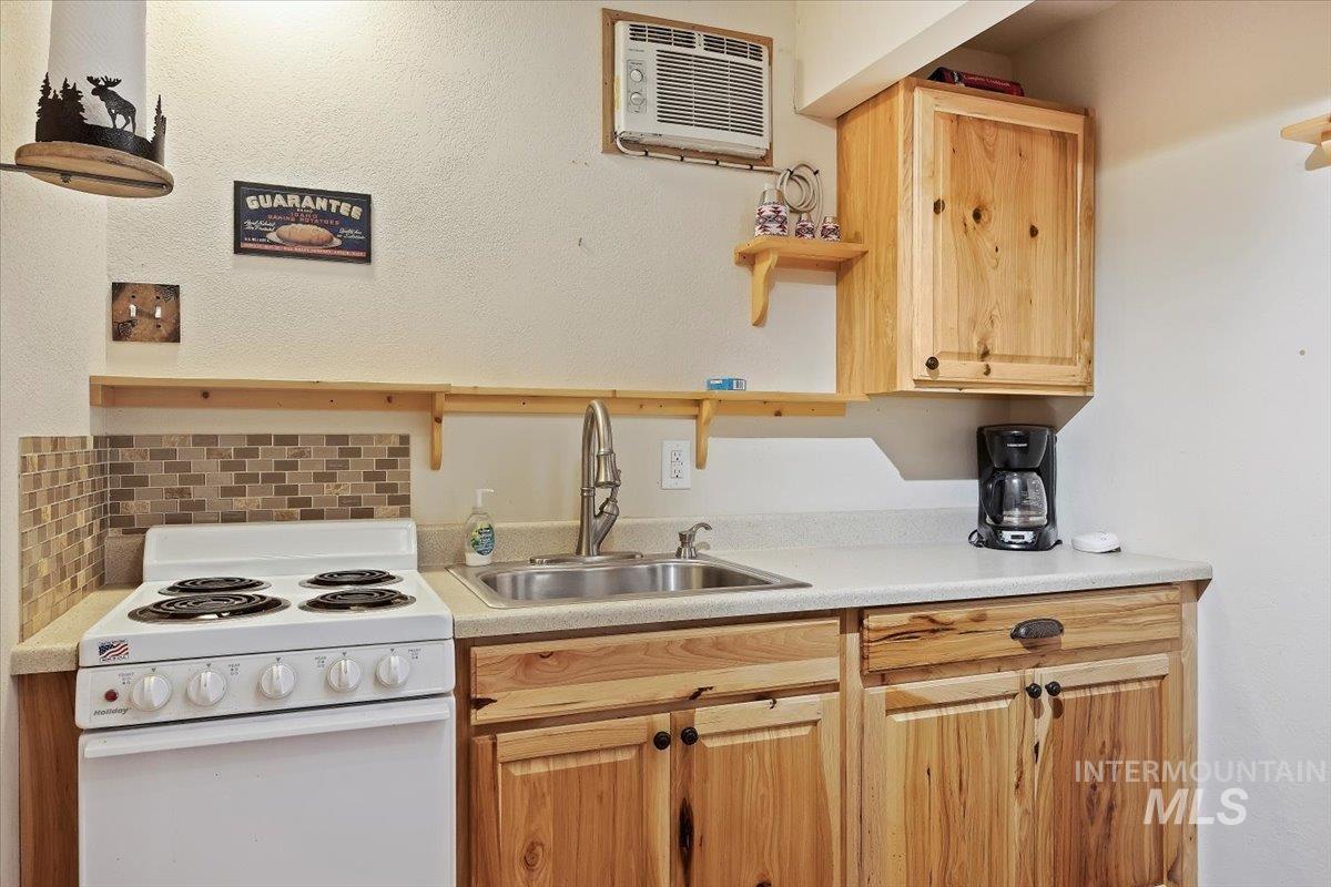 Kitchen with open shelves, electric stove, light countertops, a wall mounted AC, and light brown cabinets