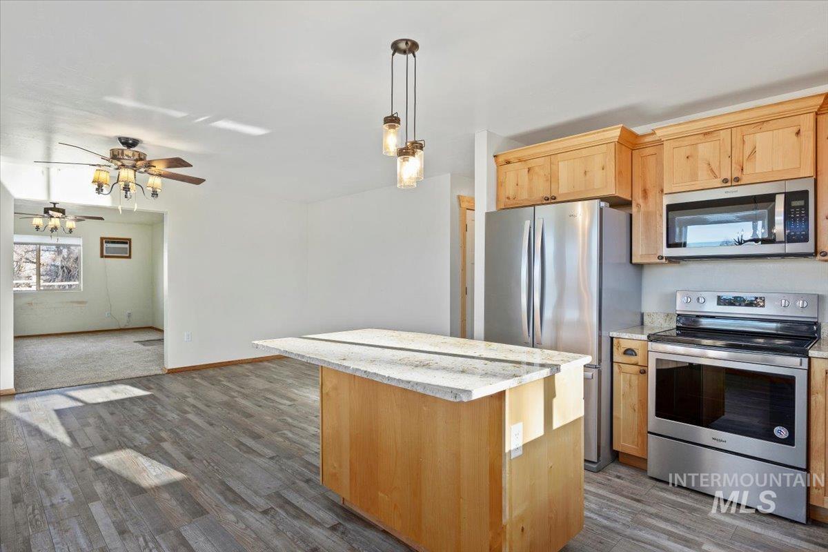 Kitchen featuring appliances with stainless steel finishes, light stone countertops, a kitchen island, a ceiling fan, and hanging light fixtures