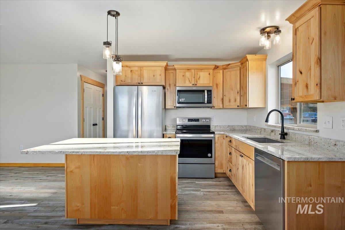 Kitchen with light brown cabinetry, appliances with stainless steel finishes, light stone countertops, and a kitchen island