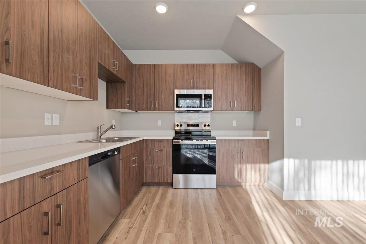 Kitchen with appliances with stainless steel finishes, light wood finished floors, modern cabinets, and brown cabinetry