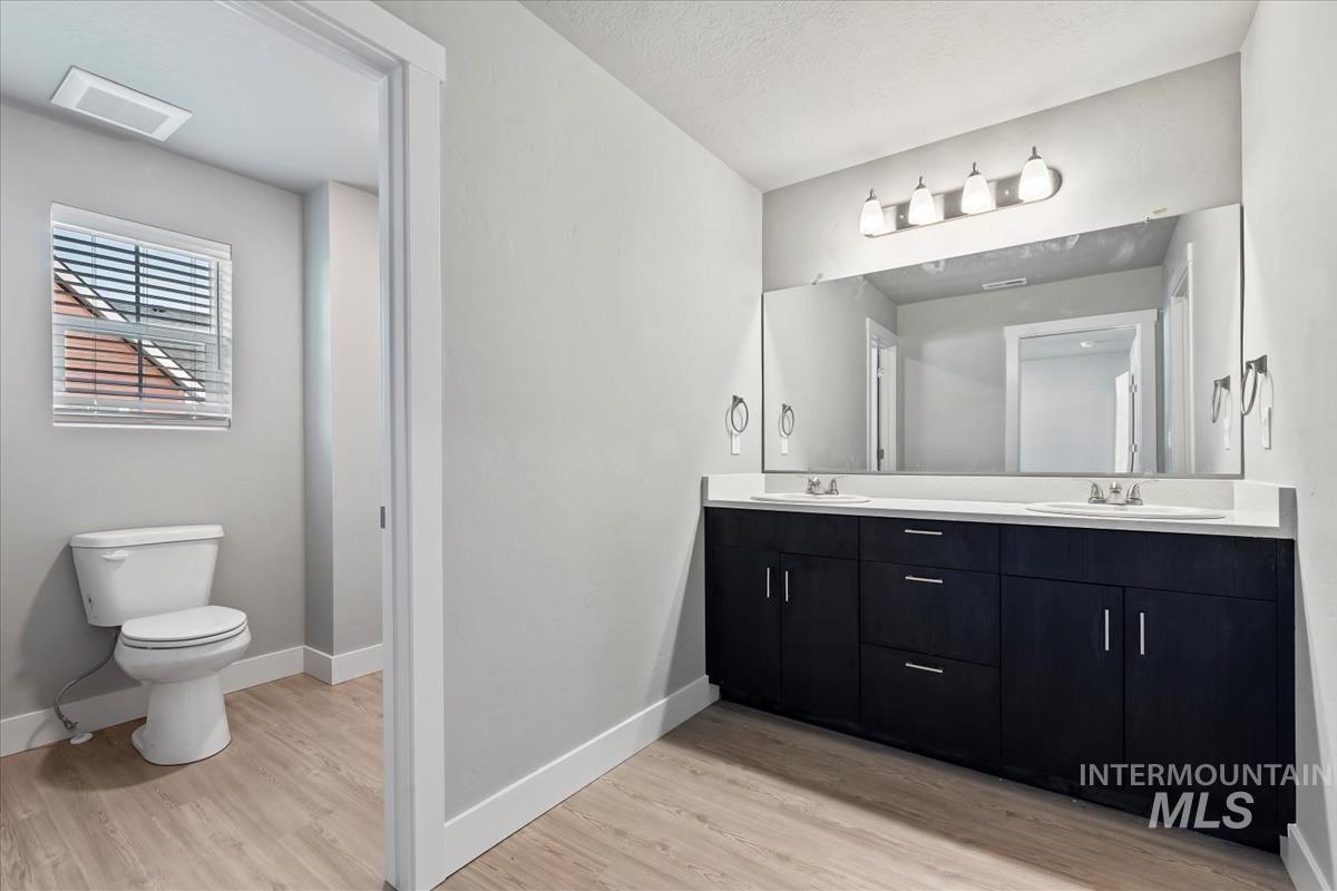 Full bath with double vanity and light wood-type flooring