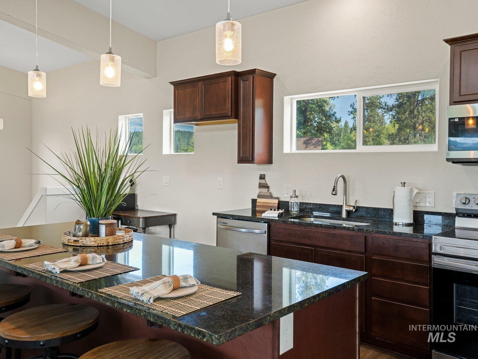 Kitchen with stainless steel appliances, dark granite countertops, dark brown cabinets, and pendant lighting
