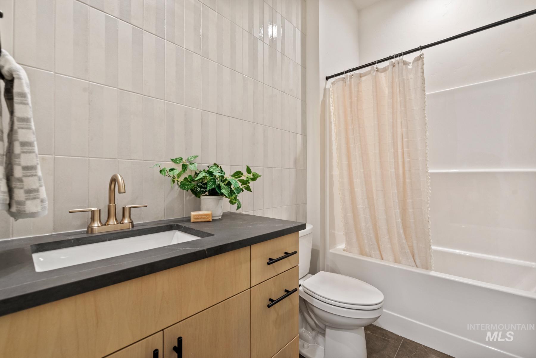 Bathroom with vanity, shower / tub combo, tile walls, and dark tile patterned flooring