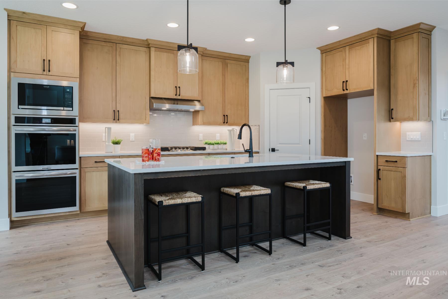 Kitchen featuring a breakfast bar, stainless steel appliances, backsplash, pendant lighting, and a kitchen island with sink
