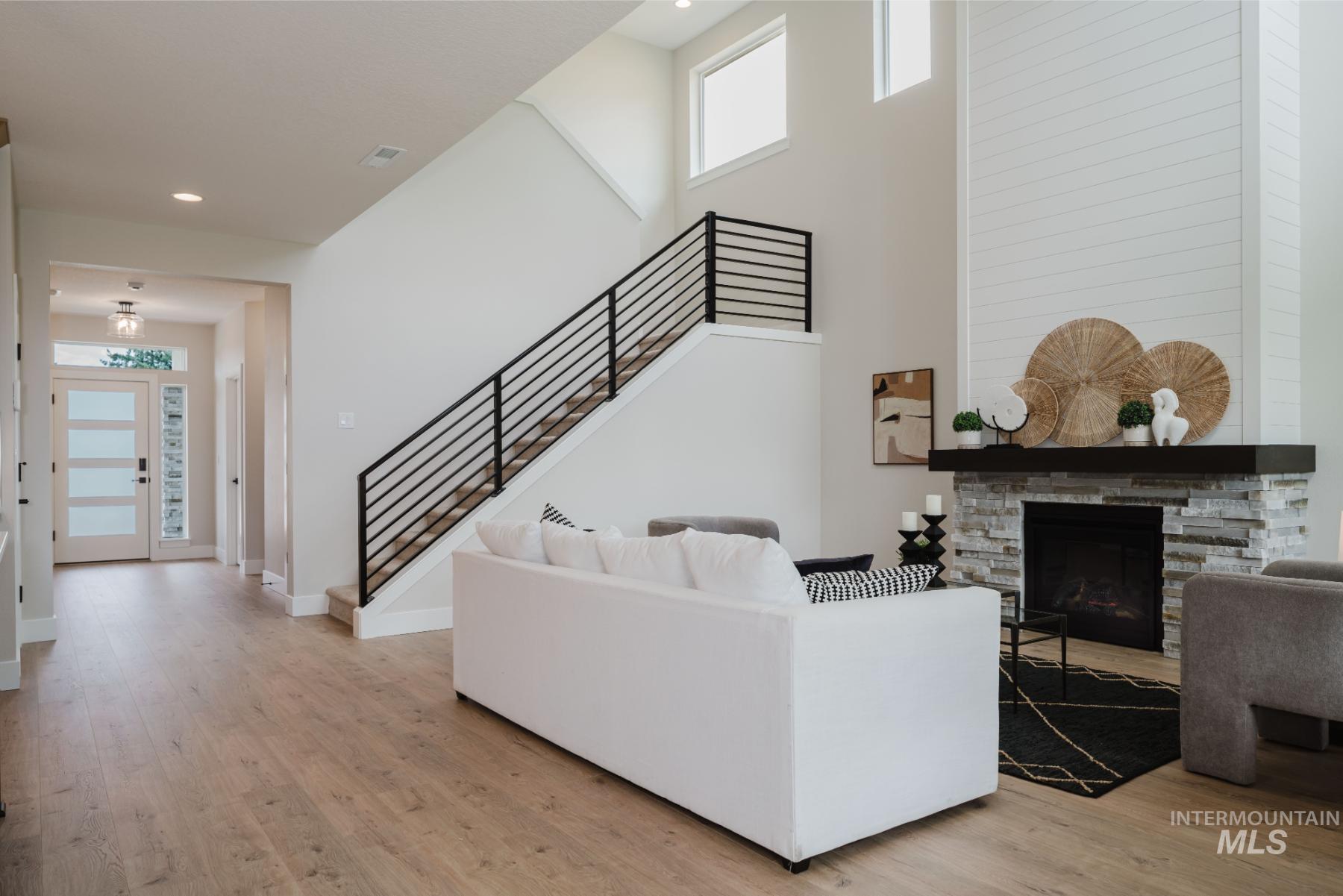 Living room with stairway, light wood finished floors, a towering ceiling, a stone fireplace, and recessed lighting