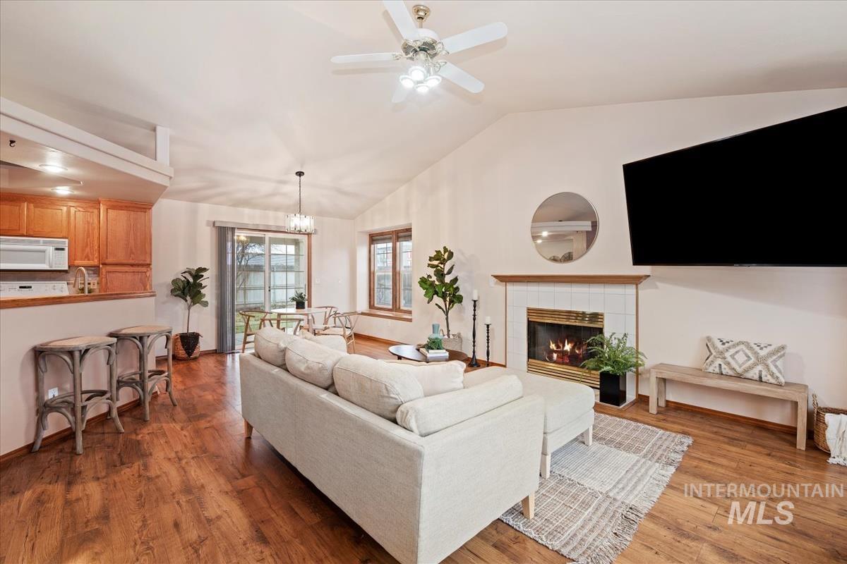 Living area with lofted ceiling, a tiled fireplace, dark wood-style floors, ceiling fan, and a chandelier