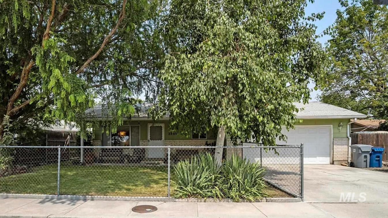 View of front of home featuring driveway, a fenced front yard, brick siding, and a garage
