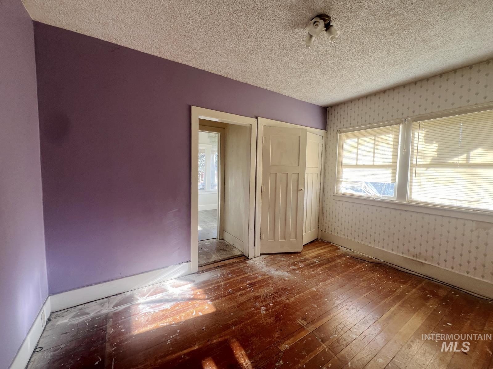 Unfurnished bedroom featuring wood-type flooring, a textured ceiling, a closet, and wallpapered walls