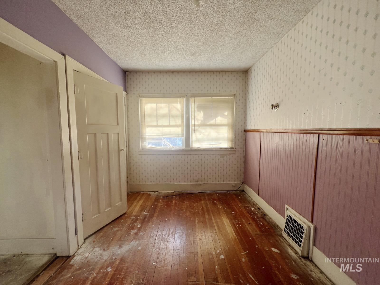 Unfurnished room with hardwood / wood-style floors, wallpapered walls, and a textured ceiling