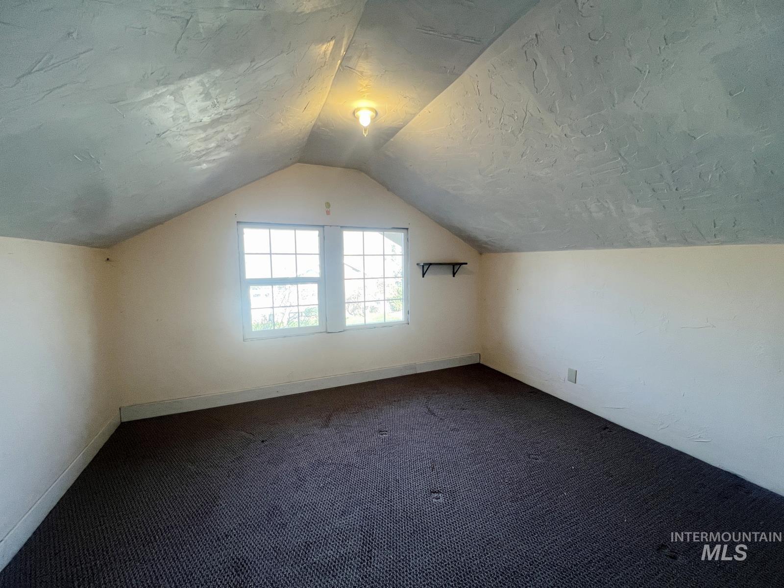 Bonus room with vaulted ceiling, dark carpet, and a textured ceiling