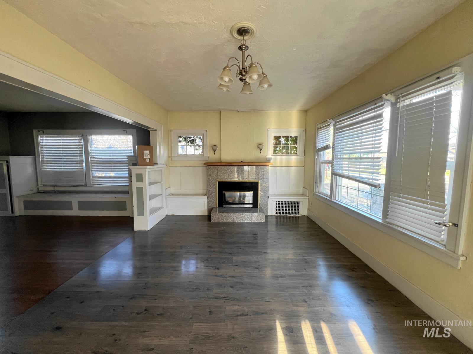 Unfurnished living room featuring dark wood-style flooring, a chandelier, a multi sided fireplace, and a textured ceiling