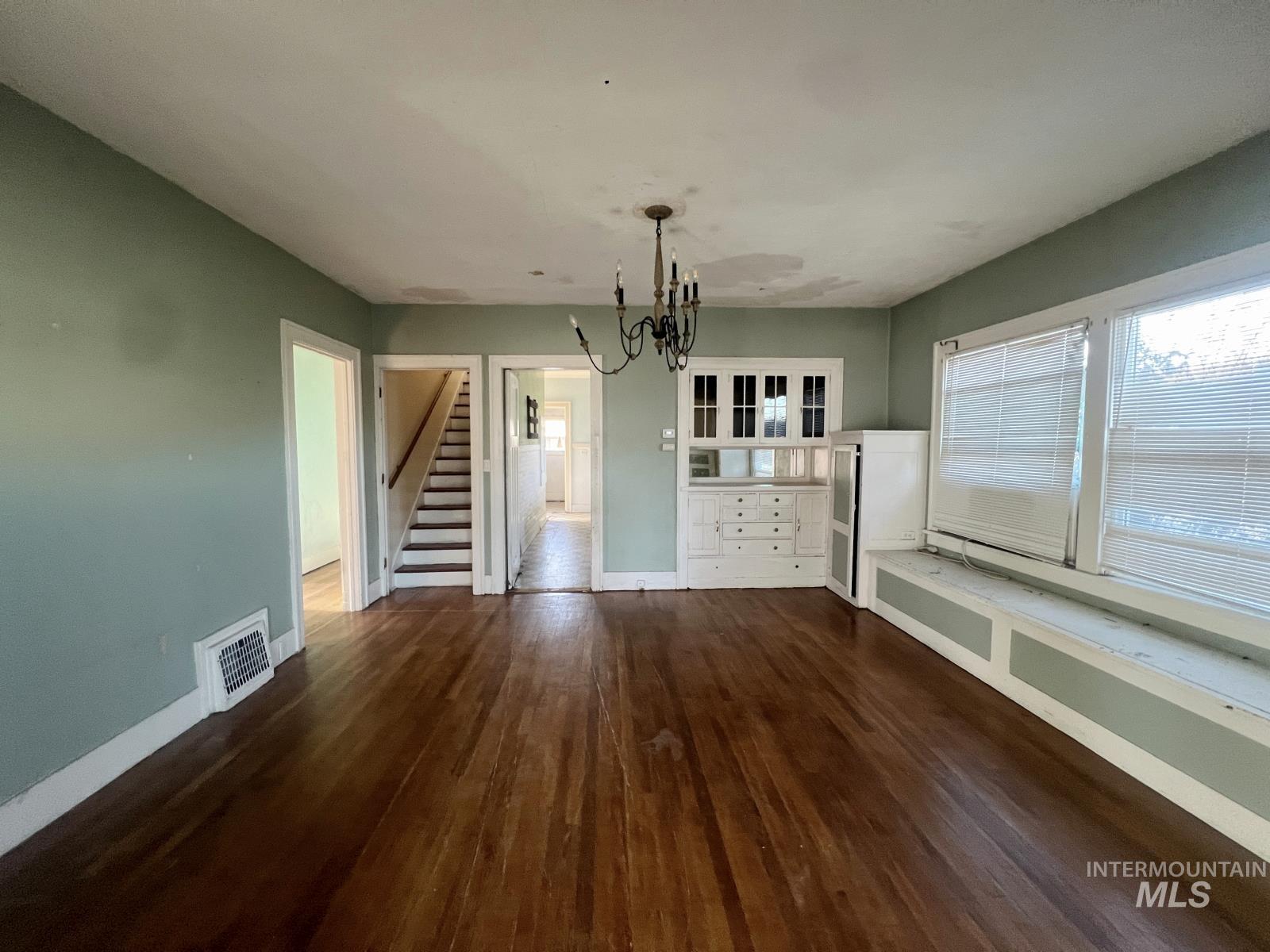 Unfurnished dining area featuring dark wood finished floors, stairway, healthy amount of natural light, and a chandelier