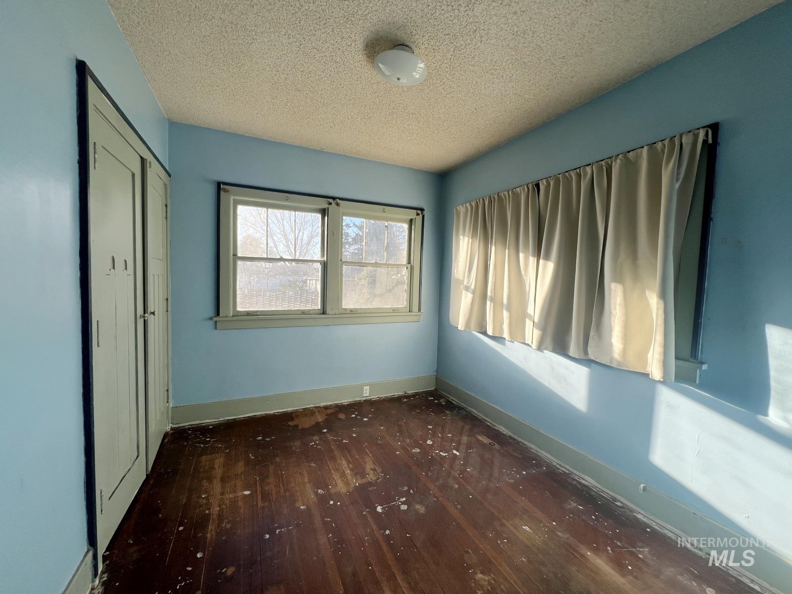 Unfurnished bedroom featuring a textured ceiling, a closet, and dark wood finished floors